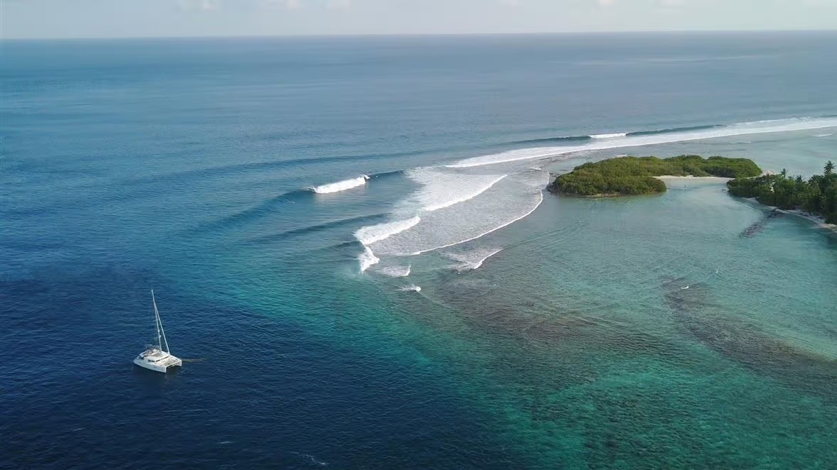 Image de la mer au maldives en vu aérienne, un catamaran en bas à droite de l'image.